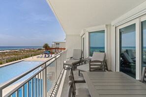A balcony with a view of the beach and ocean, lounge chairs, and a pool.