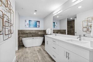 A modern bathroom with a freestanding bathtub, a large mirror, and a white vanity with drawers.
