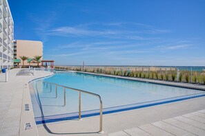Piscina azul límpida com grade de metal, área de estar coberta e vista para a praia e oceano.