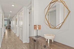 A hallway with a geometric mirror, a lamp, and a round sink on a wooden console.