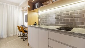 A modern kitchen with a granite countertop, white cabinetry, and a built-in oven. - Charlie Uwin Brooklin (São Paulo)