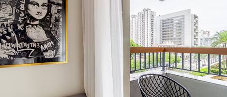 A balcony with a view of high-rise buildings, a black chair, and a framed artwork on the wall.