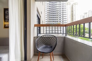 A balcony with a black wireframe chair, a wooden railing, and a view of high-rise buildings. - Charlie Uwin Brooklin (São Paulo)