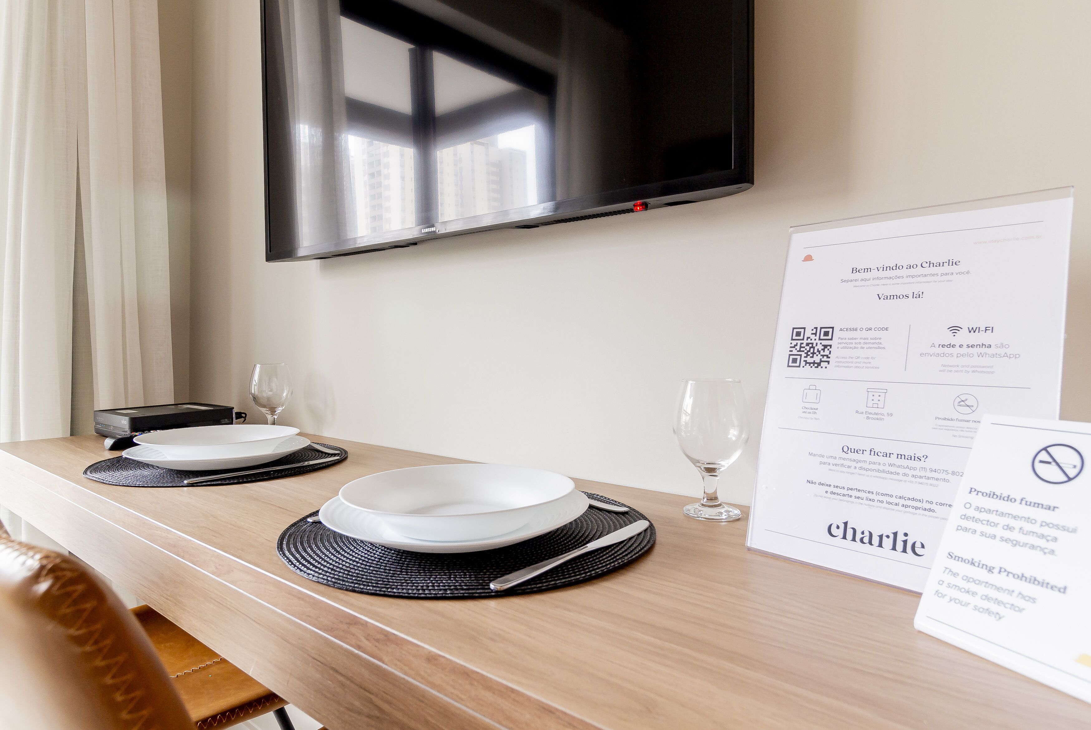Een hotelkamer met een keurig gedekte eettafel, een flatscreen televisie aan de muur en een bord met QR-codes en Wi-Fi informatie.