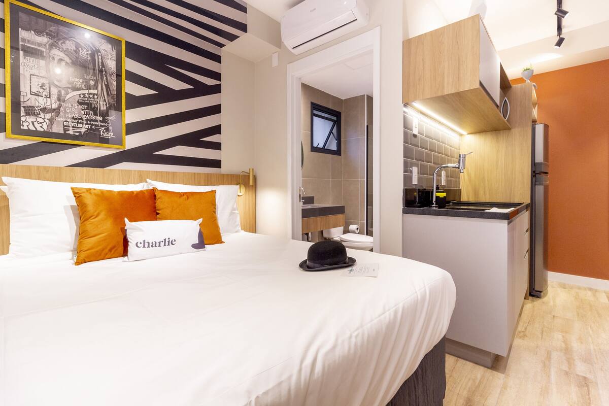 Ein Hotelzimmer mit Bett, Kopfteil, Nachttisch, Fenster, Bad und einer Küchenzeile.