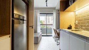 A modern kitchen with a built-in refrigerator, a dining area with a bench, and a view of a balcony with a cityscape. - Charlie Uwin Brooklin (São Paulo)