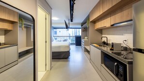 A modern kitchen with built-in appliances, a dining area, and a bedroom with a balcony. - Charlie Uwin Brooklin (São Paulo)