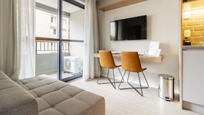 A modern hotel room with a large window, a flat-screen TV, a sofa, two chairs, and a small trash bin. - Charlie Uwin Brooklin (São Paulo)