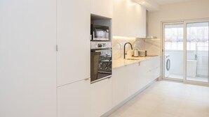 Una cocina moderna con armarios blancos, horno empotrado y un amplio ventanal con vistas a un balcón.