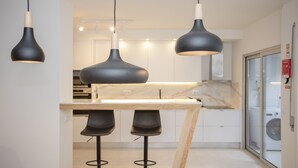 Una cocina moderna con lámparas colgantes, encimera de mármol y puerta de cristal que da a un cuarto de lavado.