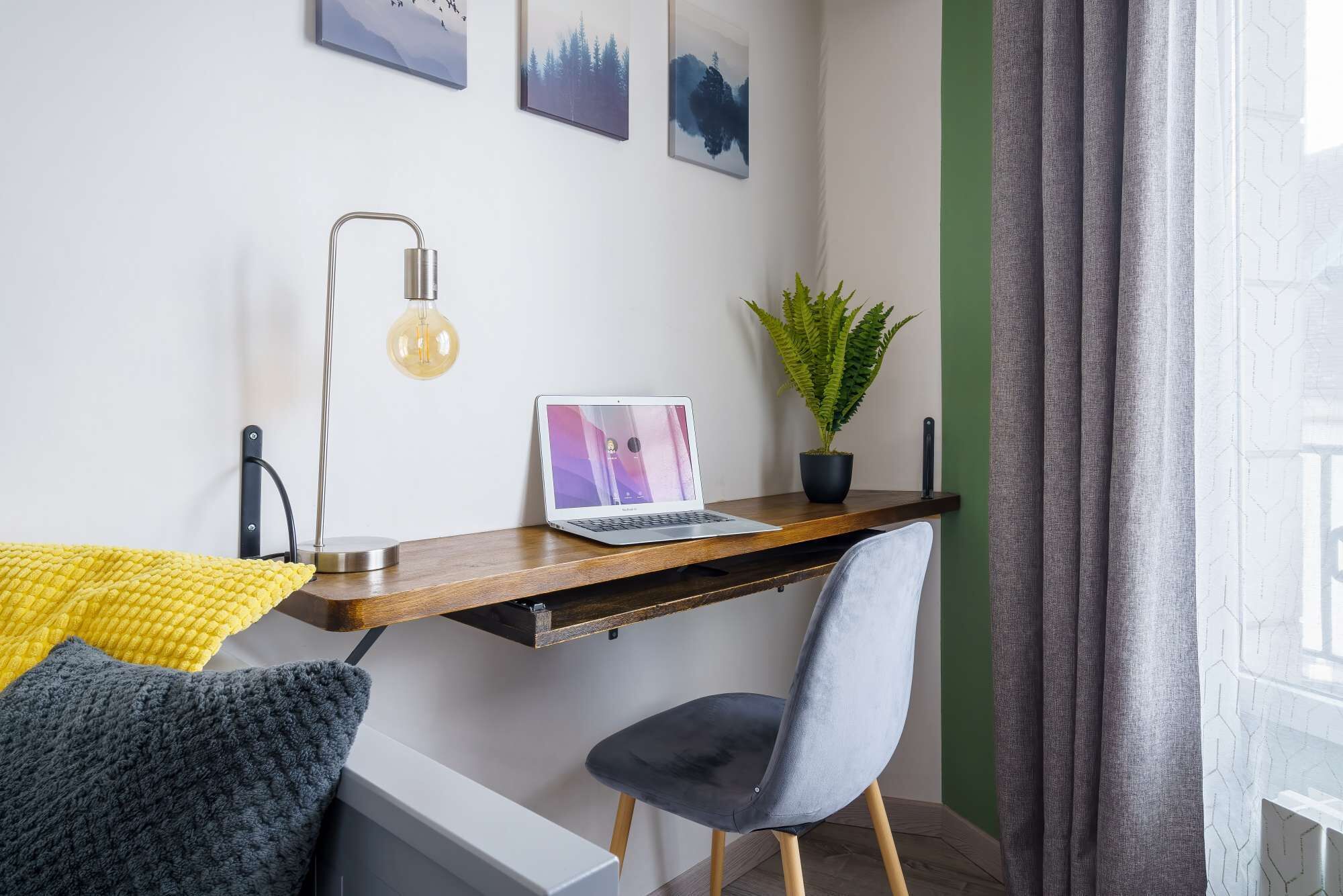 A modern workspace with a laptop, a potted plant, and a desk lamp.