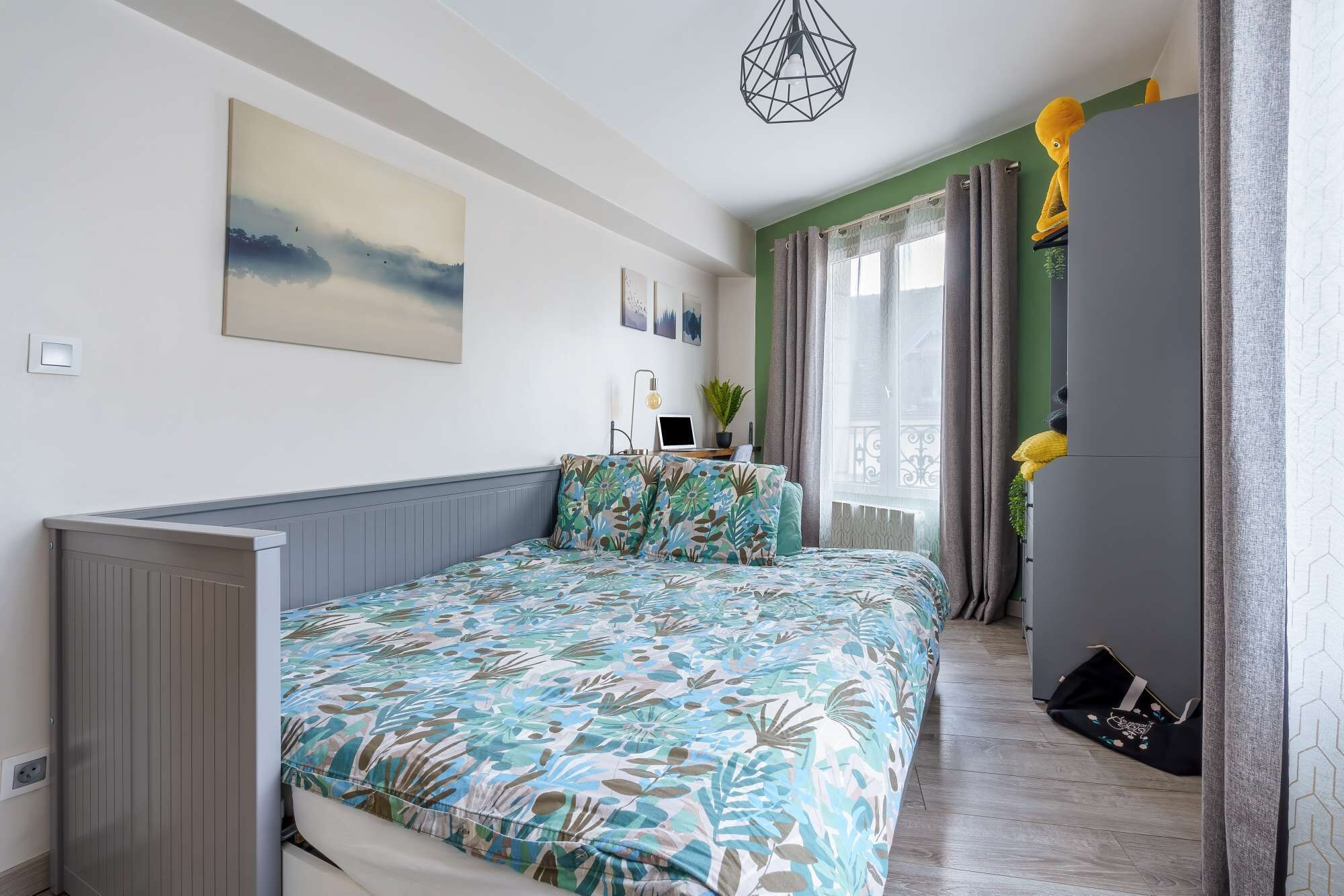Une chambre à coucher avec un lit, un bureau, une chaise, une fenêtre avec des rideaux et une plante.