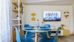 Un coin repas avec une table ronde, des chaises bleues et un téléviseur diffusant la série « MANIFEST ».