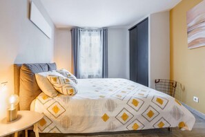 A modern bedroom with a large bed, a bedside table with a lamp, a window with curtains, and a wall-mounted artwork. - Le Saint-antoine par Your Sweet Loc (Compiègne)