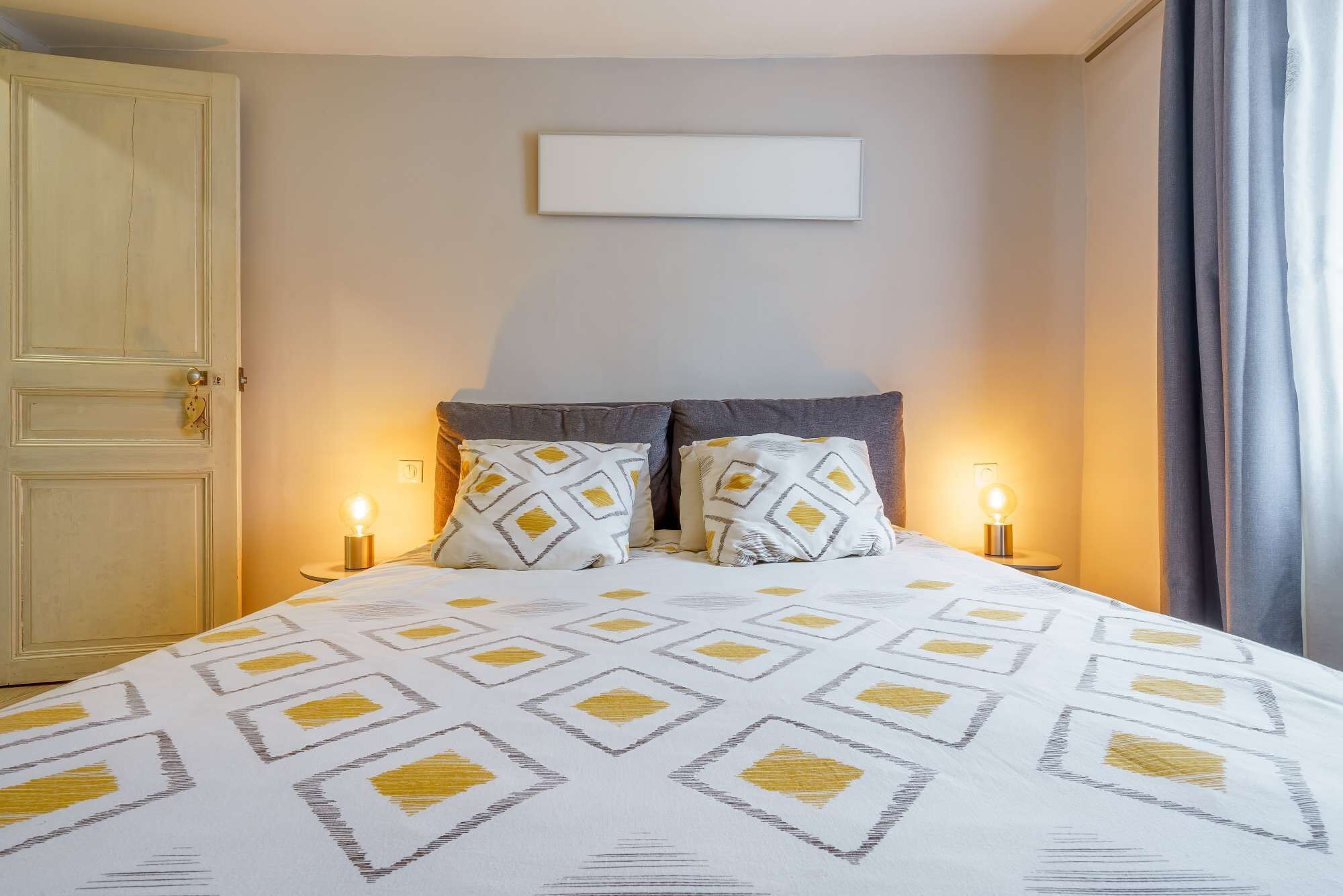 A bedroom with a bed, two bedside lamps, a door, and a wall-mounted light fixture.