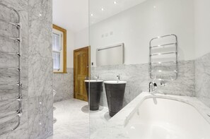 A modern bathroom with a marble floor, two sinks, a bathtub, and a wooden door. - South View House (Alnwick)