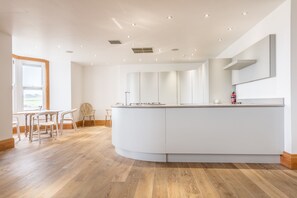 A modern kitchen with a central island, wooden flooring, and a large window providing natural light. - South View House (Alnwick)