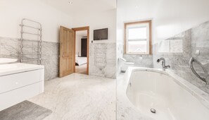 A modern bathroom with a marble floor, a large bathtub, a wooden door, and a TV mounted on the wall. - South View House (Alnwick)