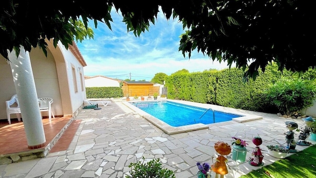 Un patio trasero con piscina, patio de piedra y mobiliario exterior.