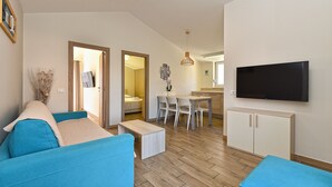 A modern living room with a blue sofa, a dining area with a table and chairs, and a TV mounted on the wall.