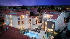A residential building with multiple balconies, a swimming pool, and a well-lit outdoor area.