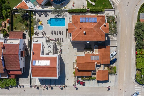 An aerial view of a residential area with a swimming pool, multiple buildings with red roofs, and a road.