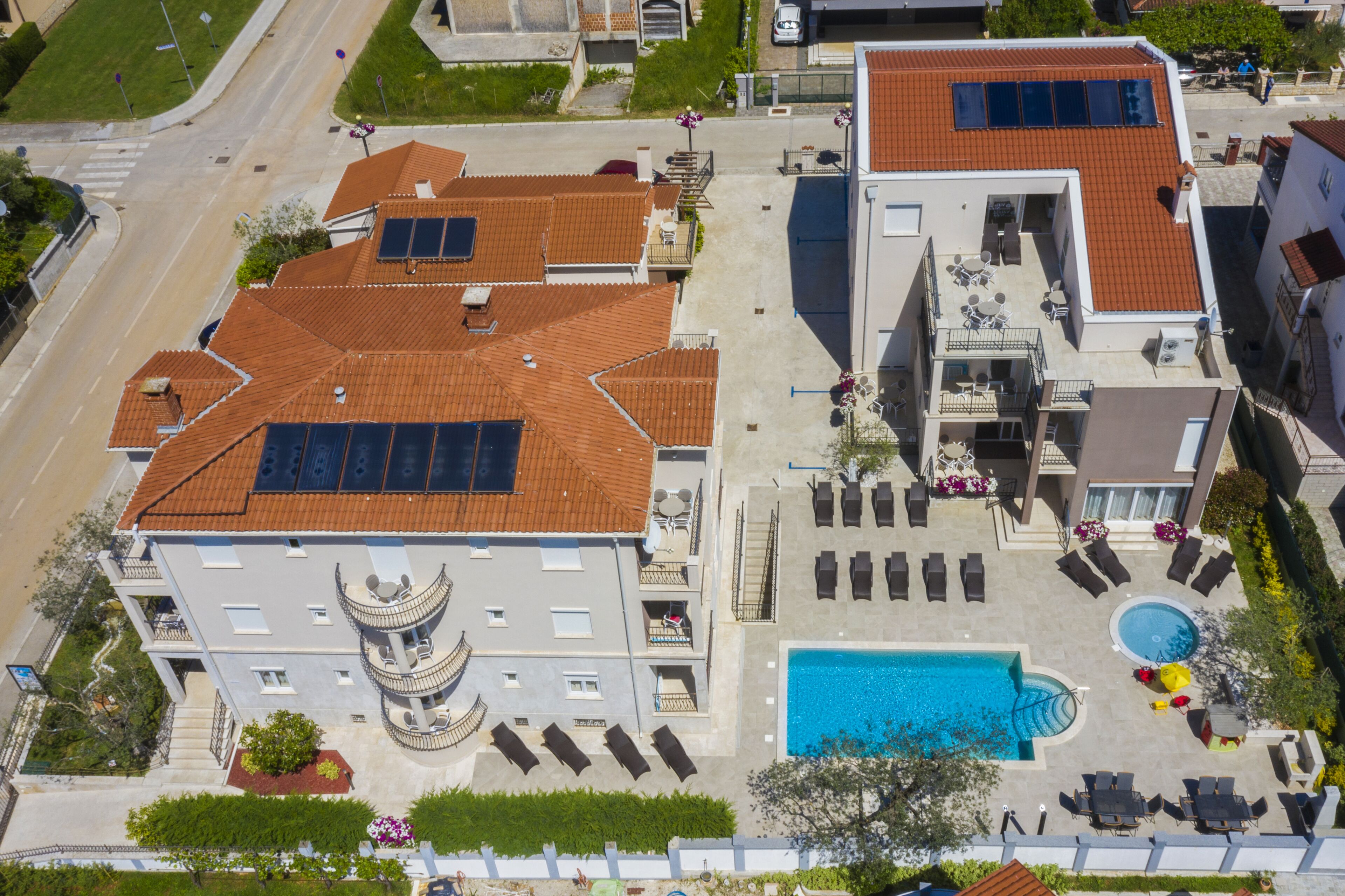 Un edificio de varios pisos con terraza en la azotea, piscina y jardín ajardinado.