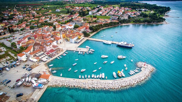 Vue aérienne d’une ville côtière avec un port de plaisance, des bateaux et un mélange de bâtiments résidentiels et commerciaux.