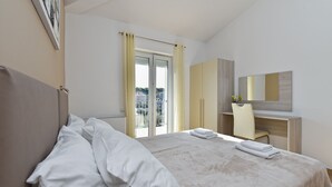 Une chambre à coucher avec un lit, un bureau, une chaise et une grande fenêtre avec des rideaux.