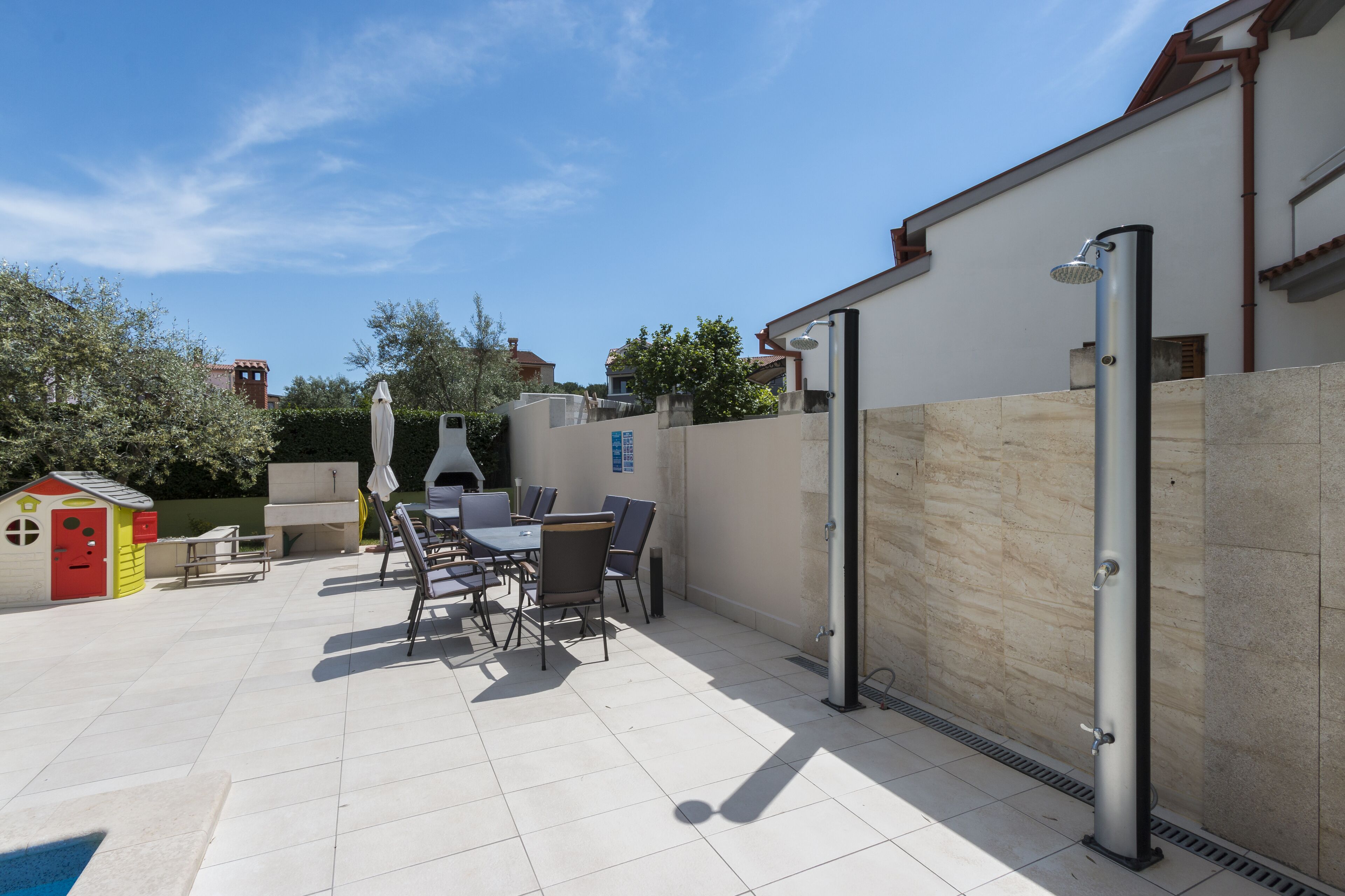 An outdoor patio with a table and chairs, a barbecue grill, and a children's playhouse.