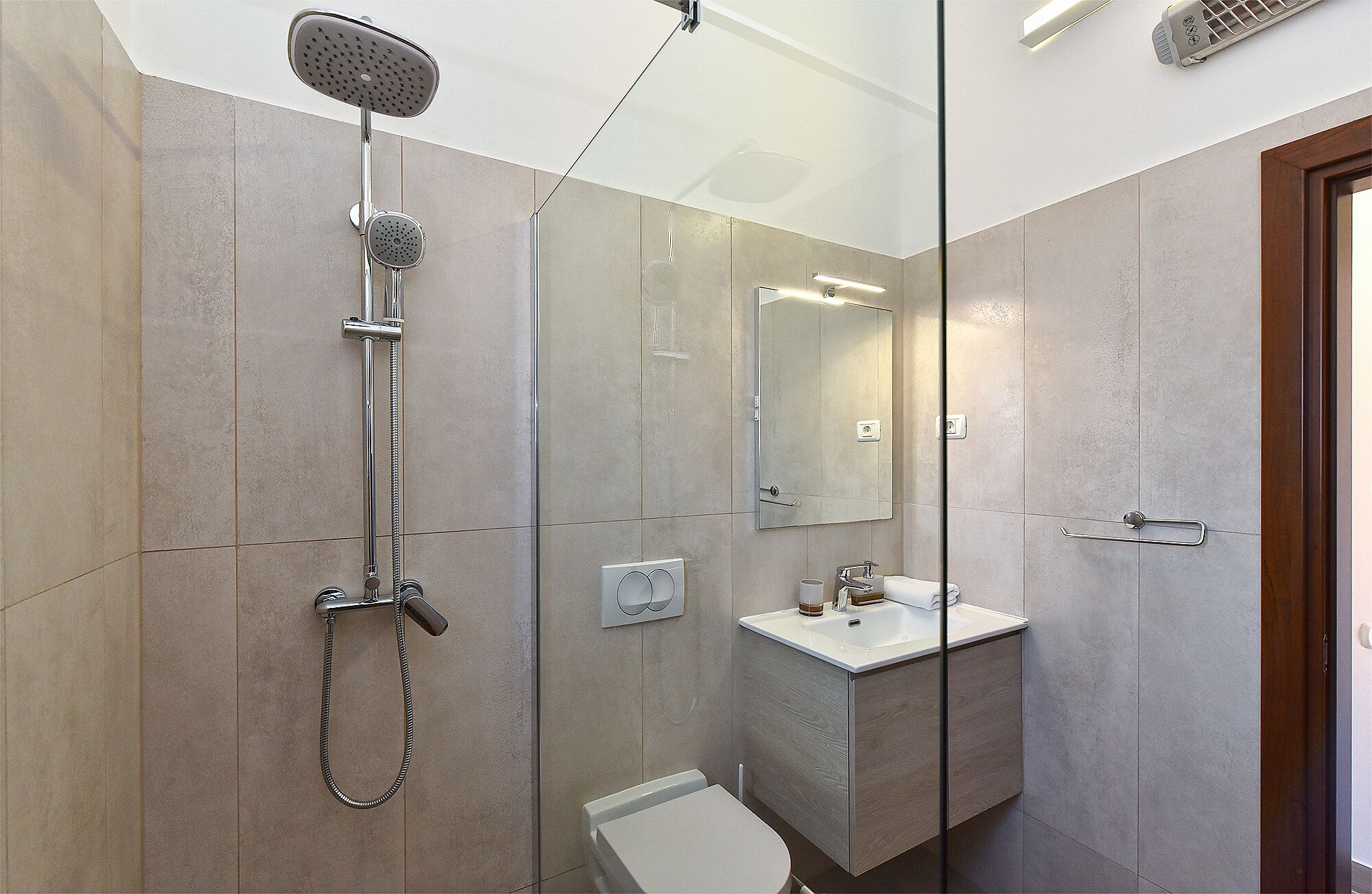 Un baño moderno con cabina de ducha de vidrio, un inodoro y un lavamanos con espejo superior.