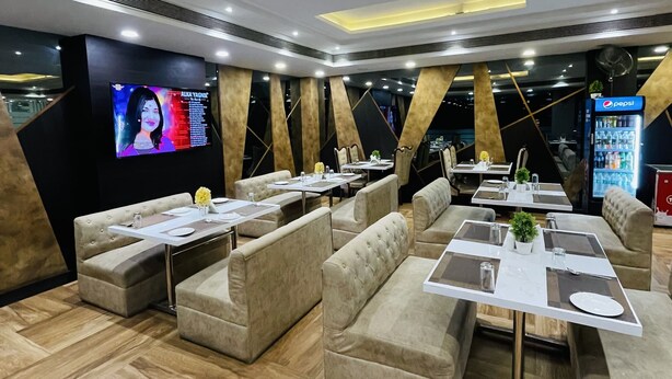 A modern restaurant interior with cushioned seating, tables set for dining, a large TV screen, and a Pepsi refrigerator. - Hotel Vijay Shree (Sohagpur)