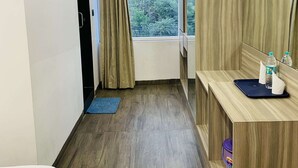 A narrow hotel room with a wooden floor, a small window with curtains, a wooden vanity with a mirror, and a blue mat on the floor. - Hotel Vijay Shree (Sohagpur)