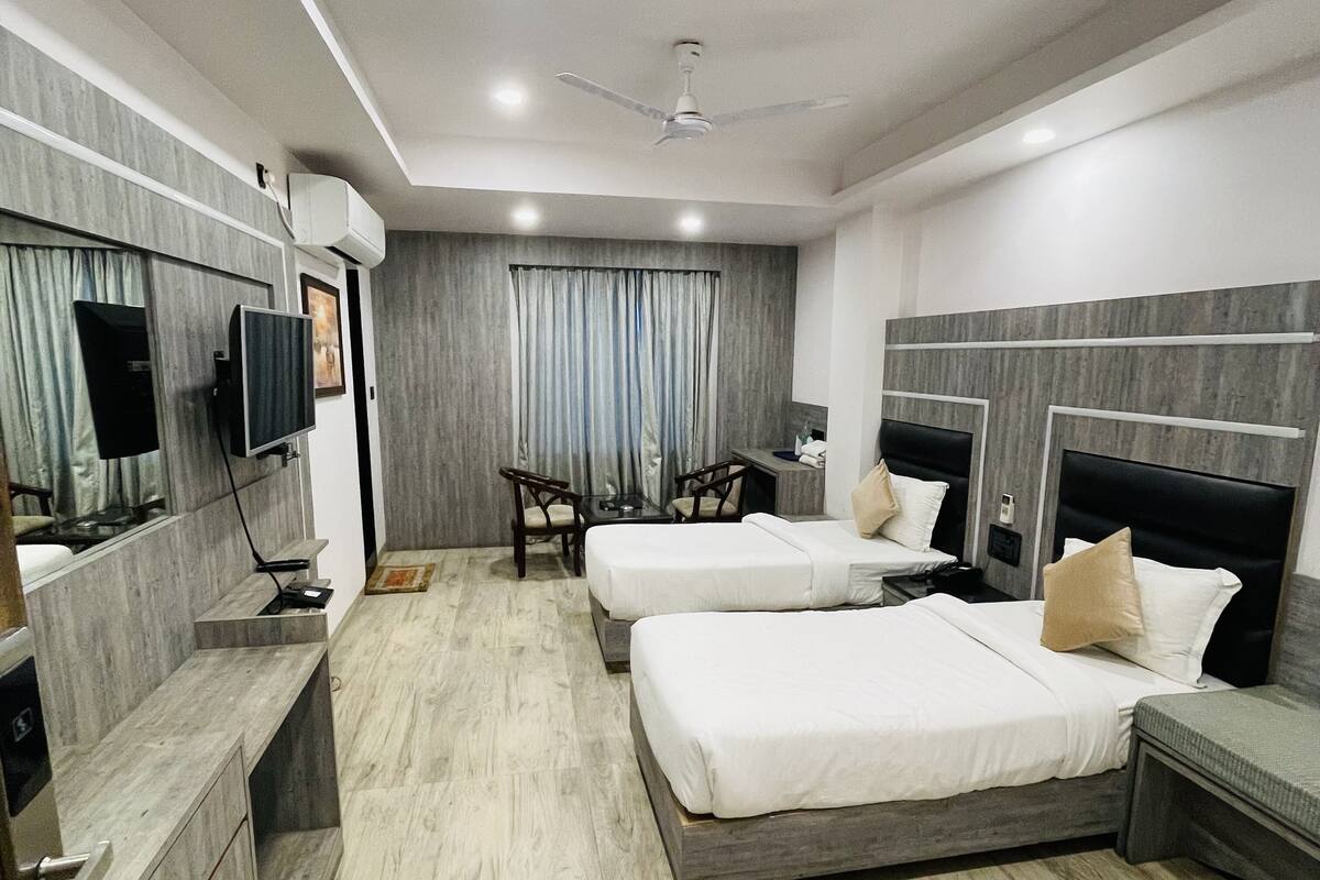 A hotel room with two beds, a desk, a chair, a TV, and a ceiling fan.