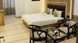 A hotel room with a bed, bedside table, chairs, a glass table, an air conditioning unit, and a painting on the wall. - Hotel Vijay Shree (Sohagpur)