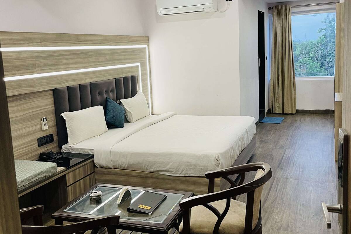 A modern hotel room with a neatly made bed, a desk with a chair, and a window with curtains.