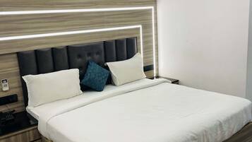 Cama bem arrumada com roupa de cama branca, cabeceira de madeira com iluminação embutida, telefone ao lado da cama e ar condicionado na parede.