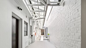 A narrow, white-walled corridor with a skylight, a door, and a small table with a plant. - Azzurro Boutique Hotel - Surry Hills (Darlinghurst)