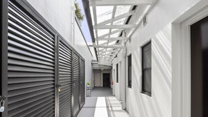 A narrow corridor with closed shutters on one side and a white wall on the other, leading to a door at the end. - Azzurro Boutique Hotel - Surry Hills (Darlinghurst)