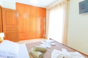 A hotel room with a bed, a wooden wardrobe, a coat rack, and towels.