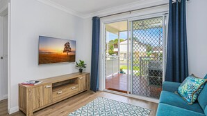 Een woonkamer met een tv-meubel van hout, een blauwe bank en een groot raam met uitzicht op een woonwijk.