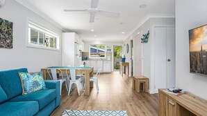 Een moderne woonkamer met een blauwgroene bank, een houten eettafel en een plafondventilator.