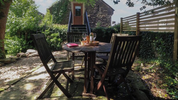 An outdoor seating area with a stone building in the background, surrounded by greenery. - The Stables (Colne)