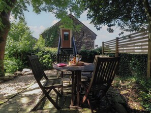 An outdoor seating area with a stone building in the background, surrounded by greenery. - The Stables (Colne)