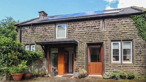 A stone house with a solar panel roof, a wooden front door, and a cobblestone driveway. - The Stables (Colne)