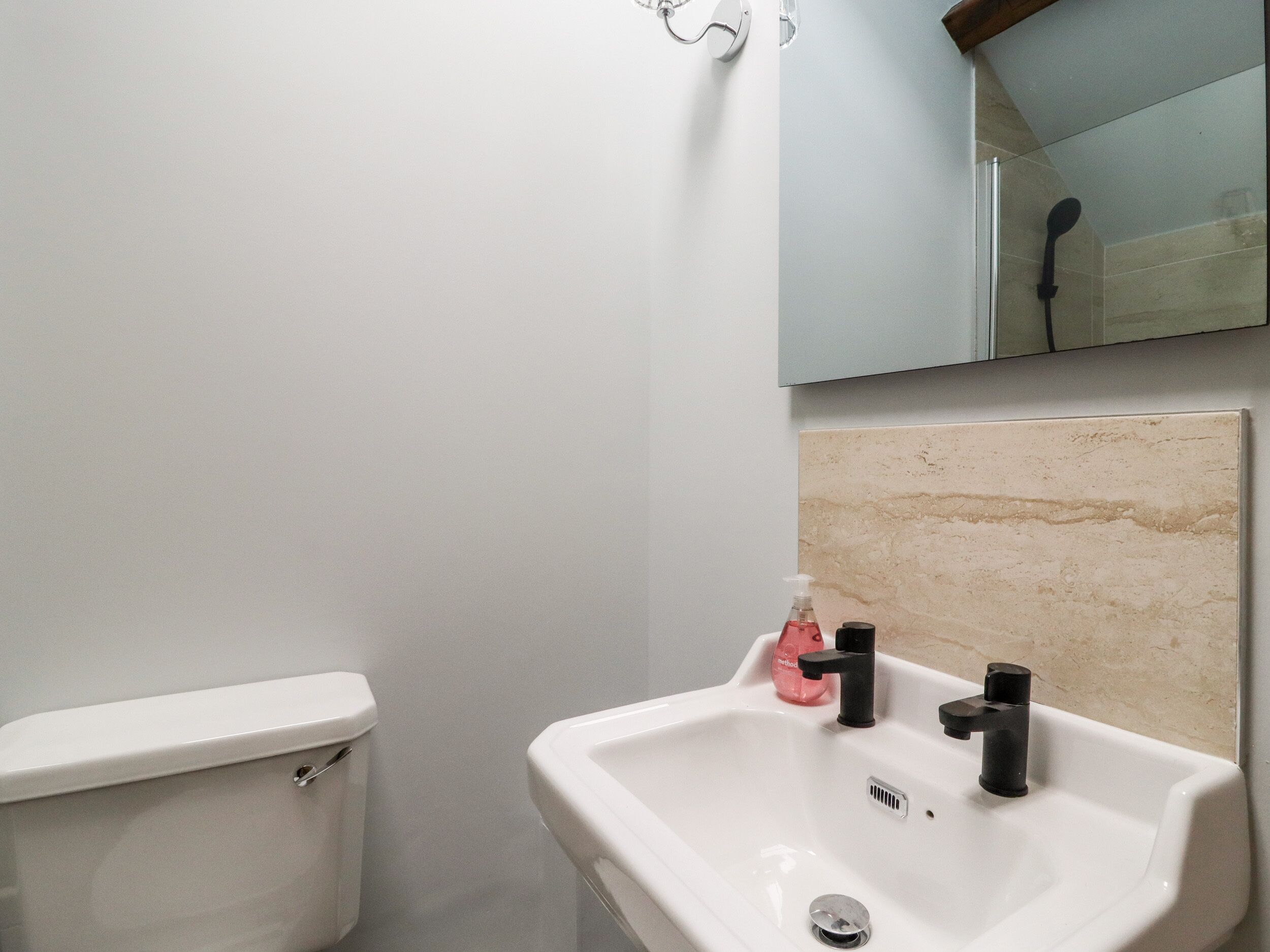 A bathroom with a toilet, a sink with a mirror above it, and a shower area.