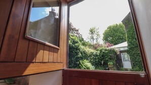 A wooden door with a window, revealing a garden with various plants and a white building in the background. - The Stables (Colne)