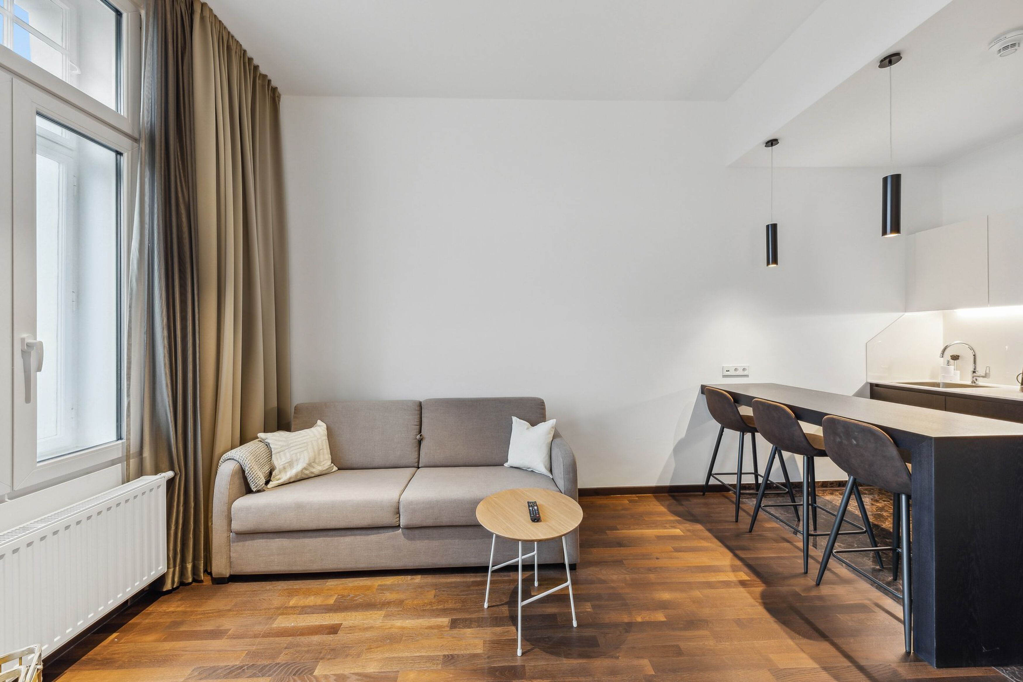Ein modernes Wohnzimmer mit einer Couch, einem runden Couchtisch und einer Küchenzeile mit einer Bartheke und Stühlen.
