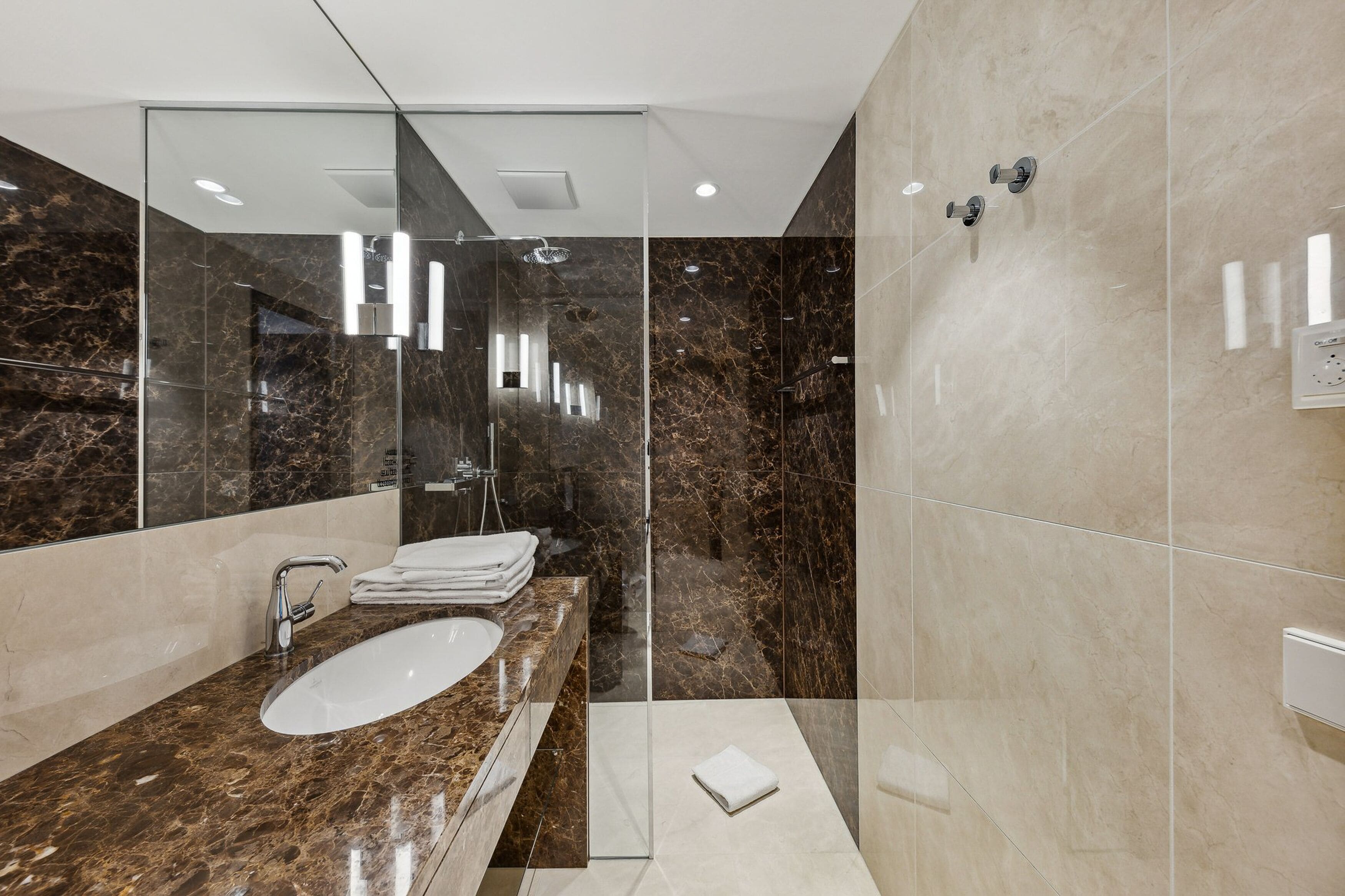 Un baño moderno con ducha de vidrio, tocador de mármol y un espejo grande.