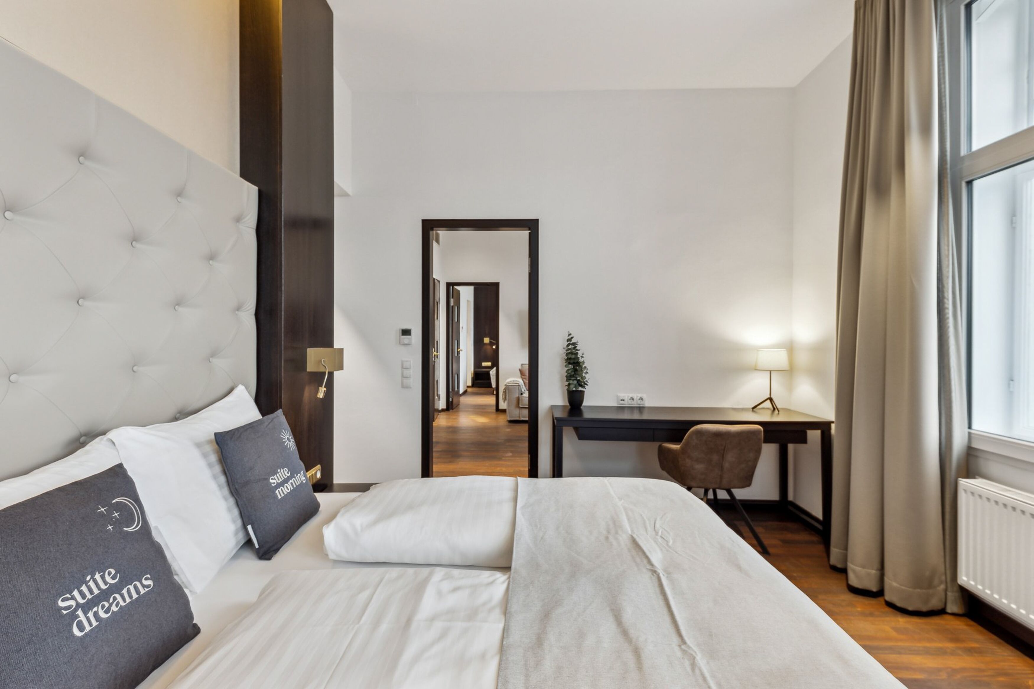 Habitació d'hotel amb un llit gran, una taula, una cadira i vista al passadís.